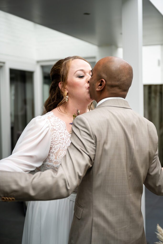 a bride and groom kiss with their hands clasped and their arms spread wide
