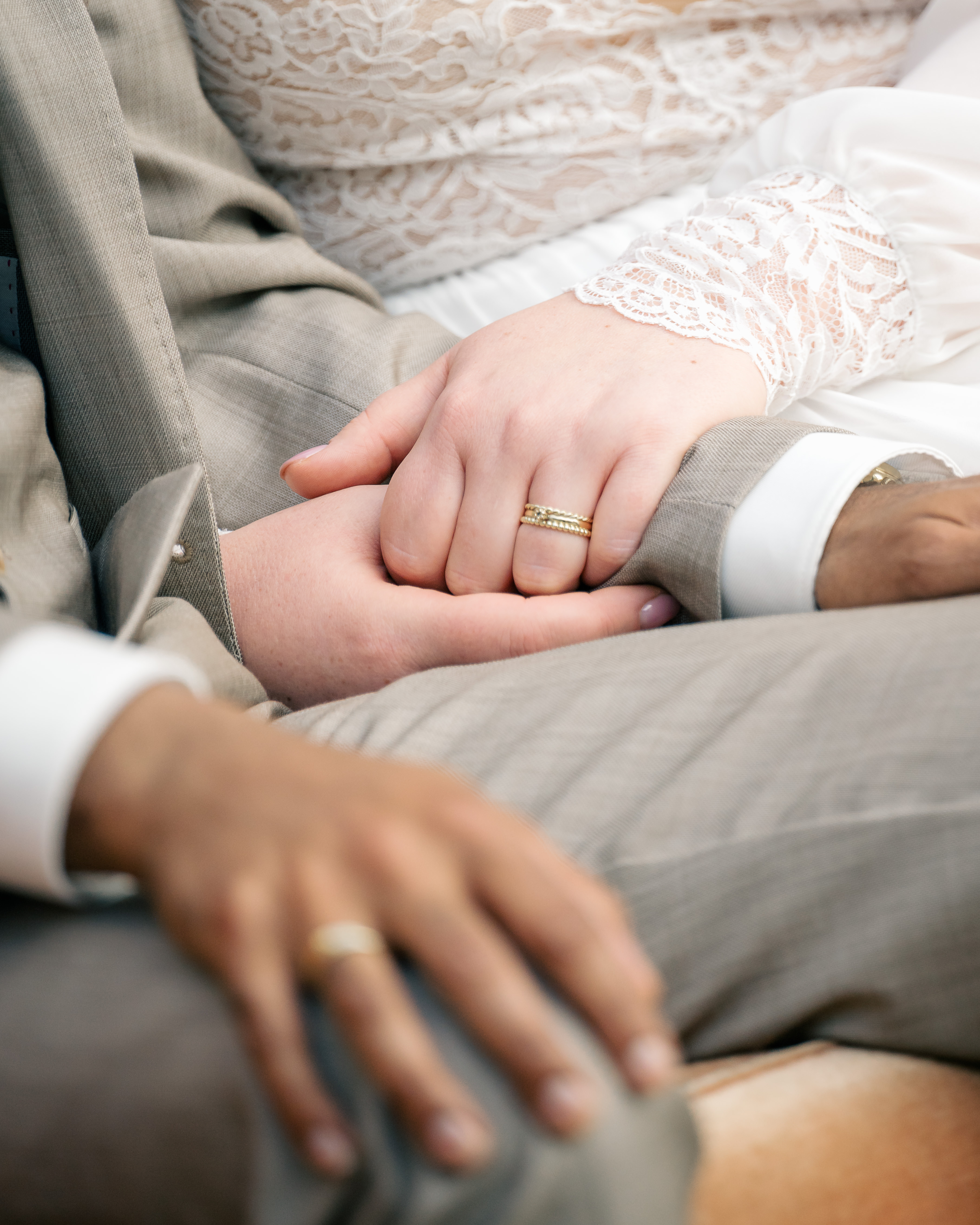 detail shot of bride holding the arm of the groom in both hands with her wedding ring in focus and groom's other hand on his knee