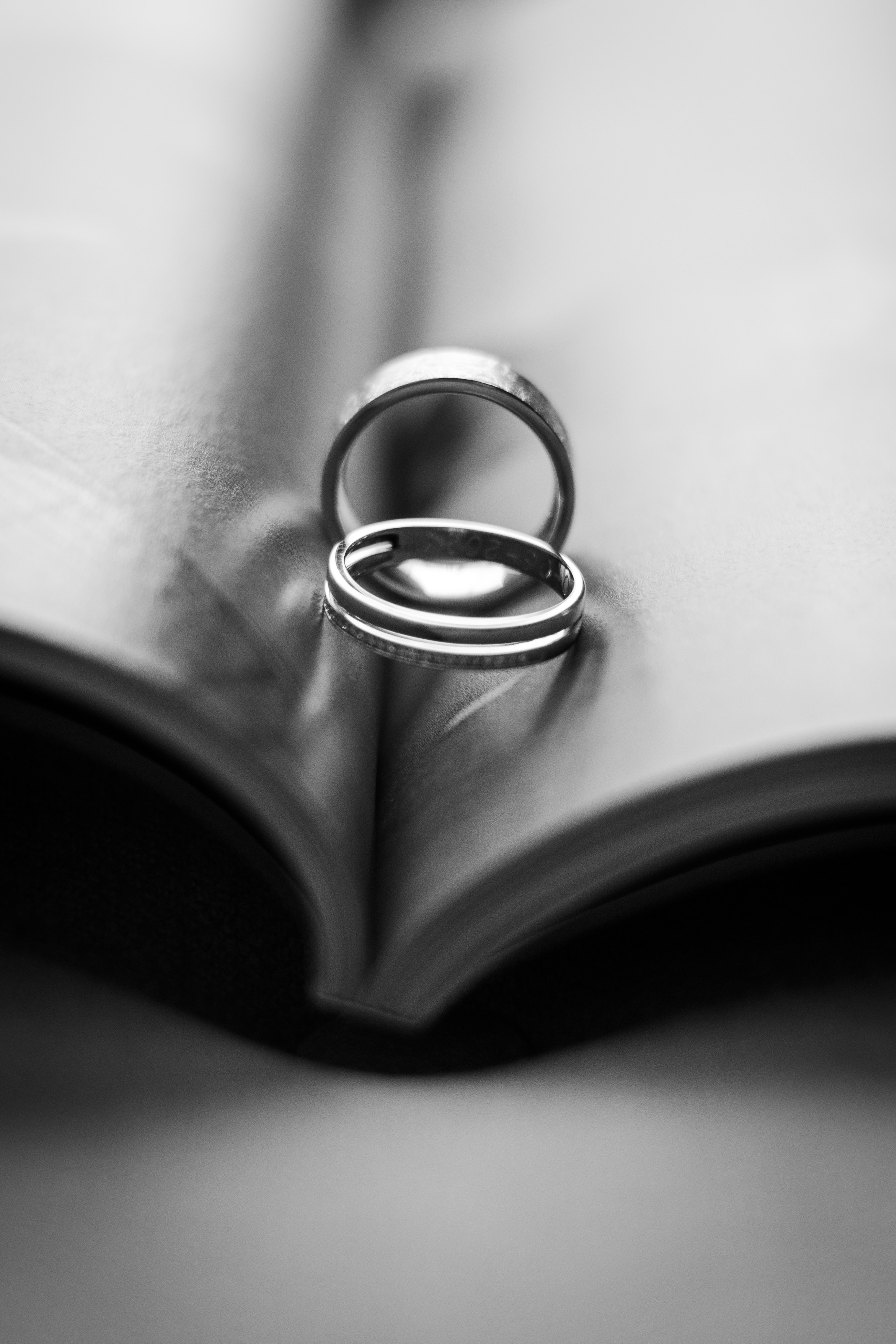 black and white detail shot of two wedding rings sitting and standing upright in the folds of a hotel magazine