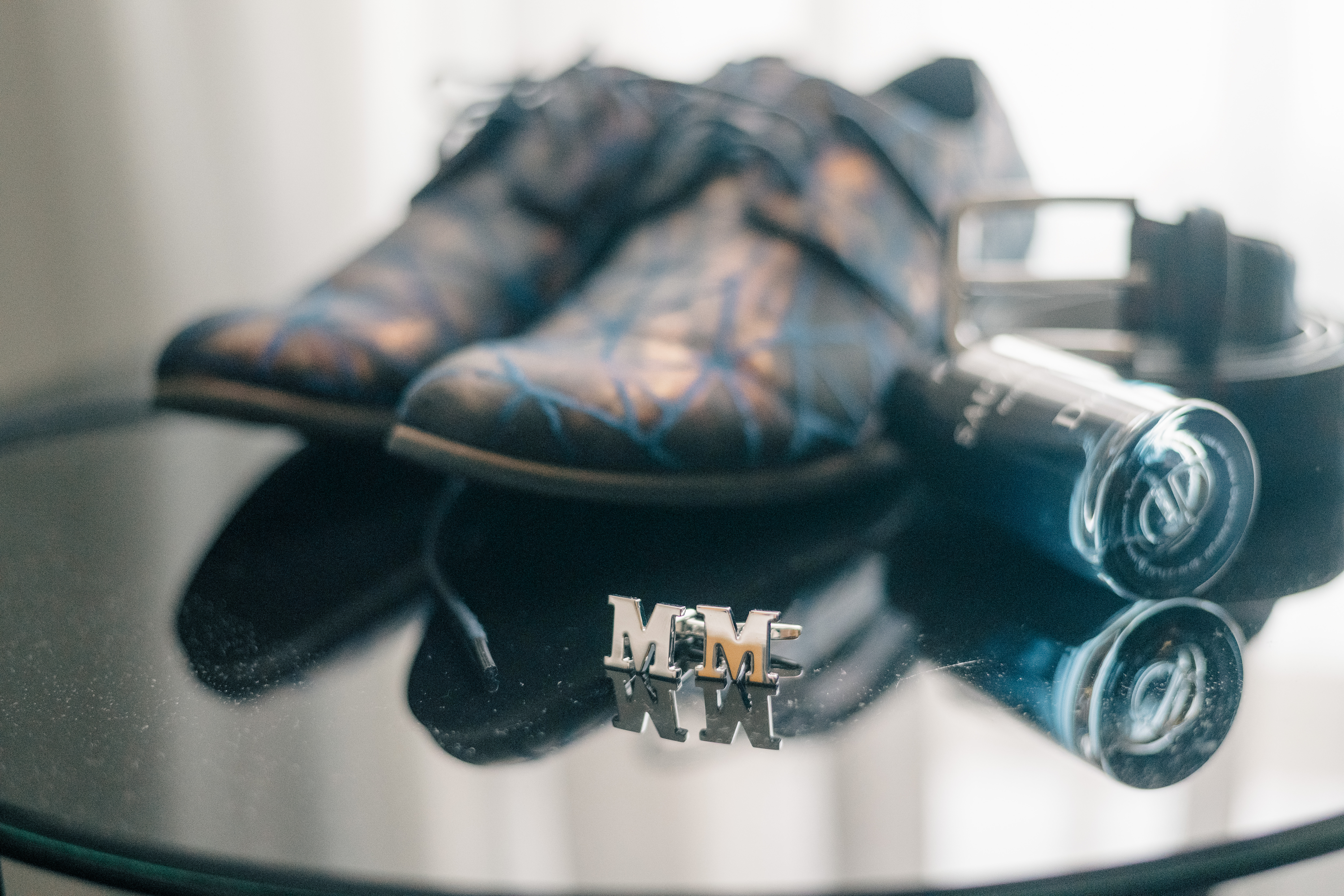 Grooms detail shot of cufflinks and shoes on a reflective glass table