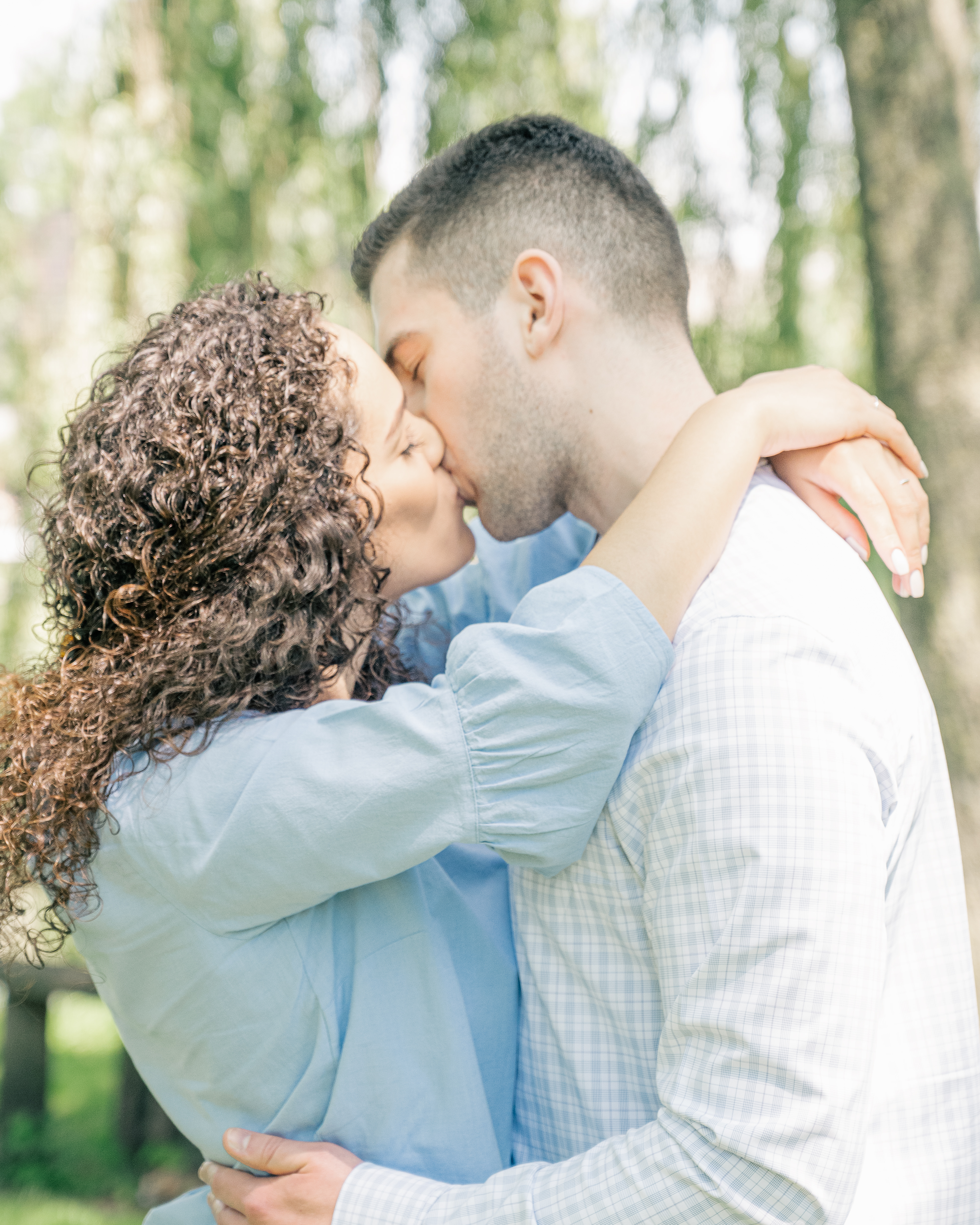 Engagement photo of fiancés kissing wearing blue and standing under a willow tree