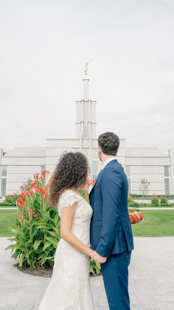 A bride and groom hold hands and face towards the spire of the Hague Netherlands Temple, a wedding venue near me
