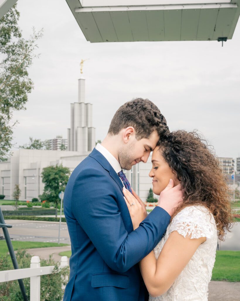 A bride and groom stand on a Dutch style bridge with the Hague Netherlands temple behind them in sight