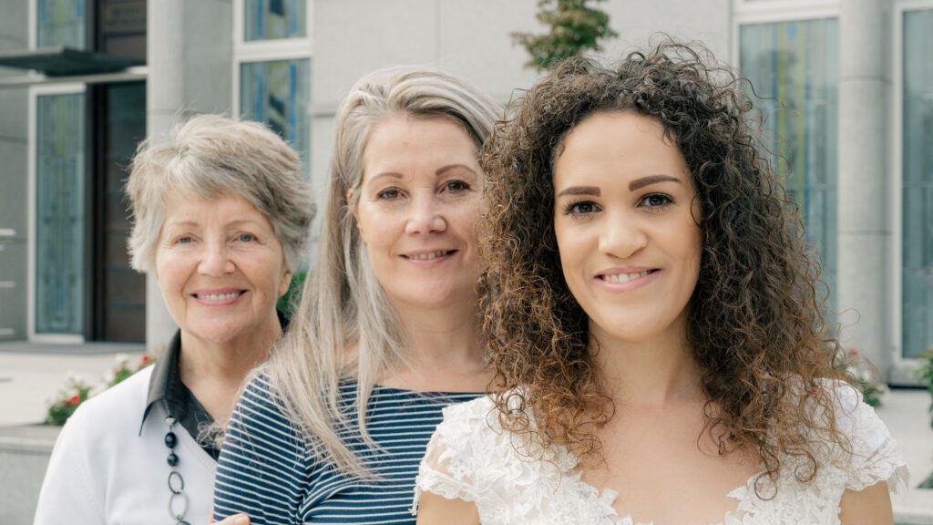 Three generations of bride, mother of the bride, and grandmother of the bride stand in front of a Church of Jesus Christ Temple
