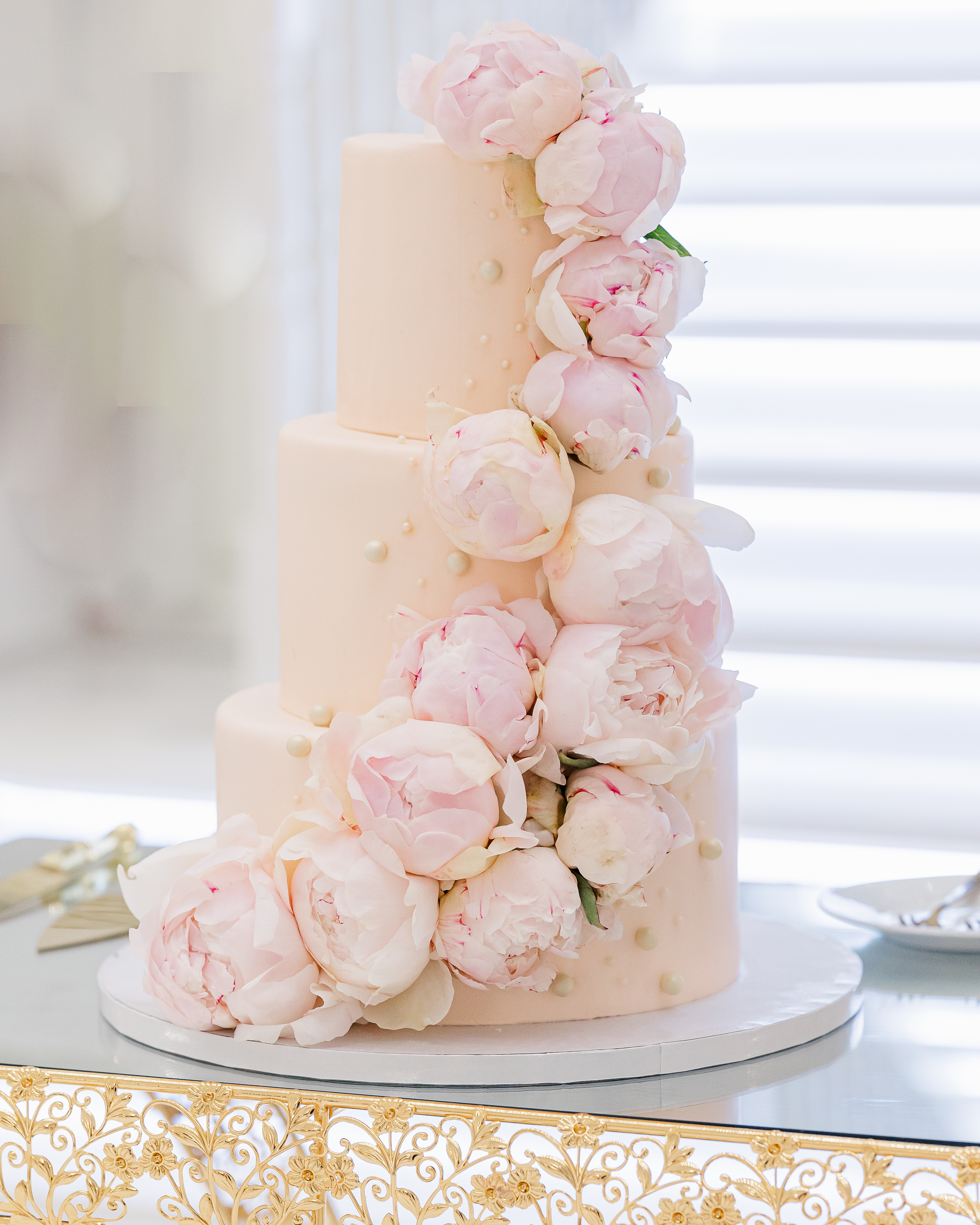 Wedding cake detail shot of a pink three tier wedding cake bedecked with peonies and gold dots