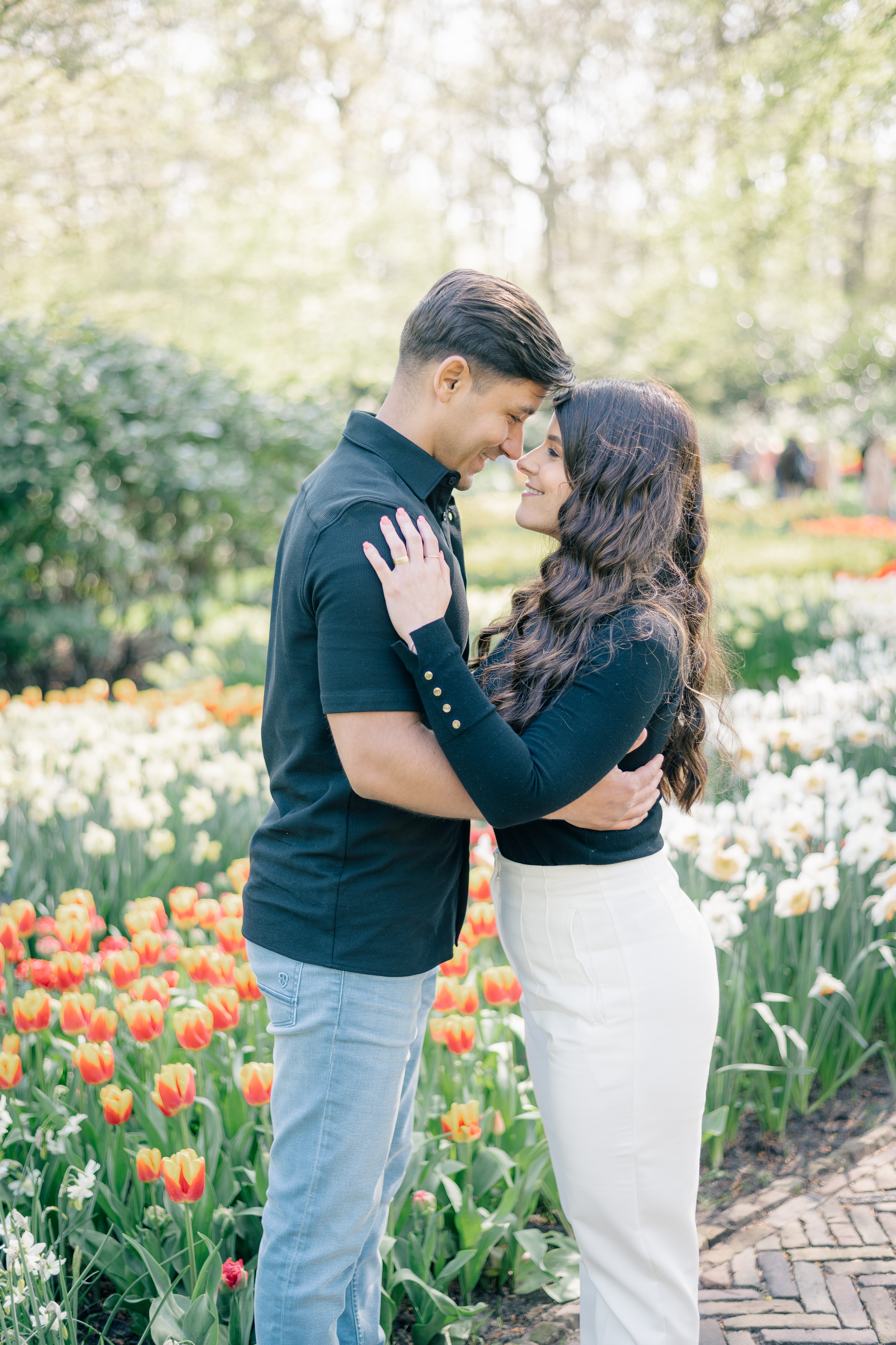 A woman and a man stand facing each other nose to nose in front of several flower beds in the Keukenhof garden
