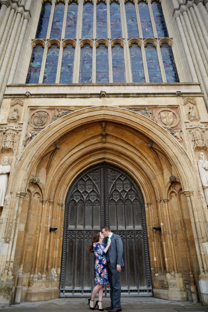 A man and a woman stand and kiss at the doors of Norwich Cathedral