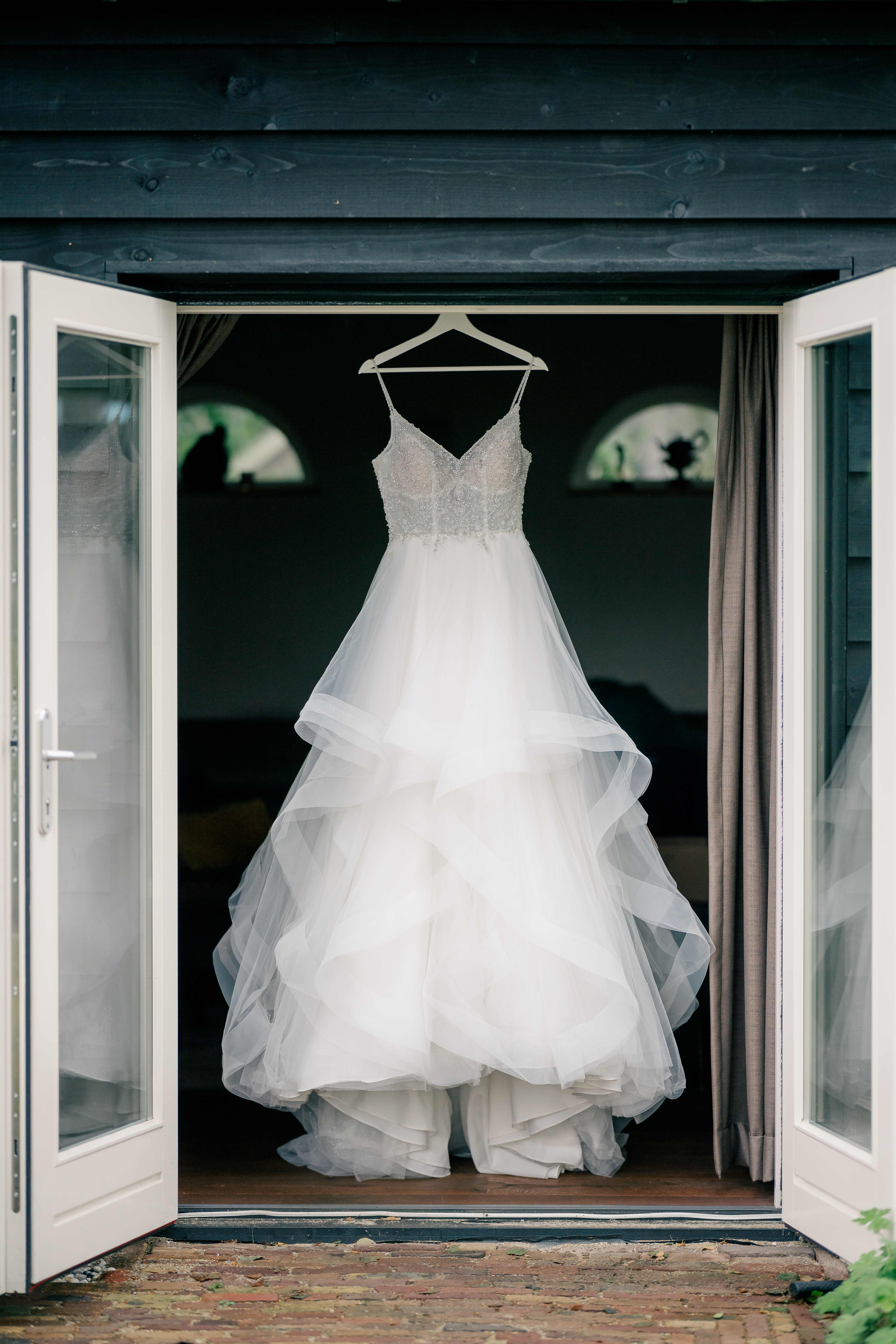 View of a sleeveless white wedding dress hanging in the double door garden entry of a home in Heerle