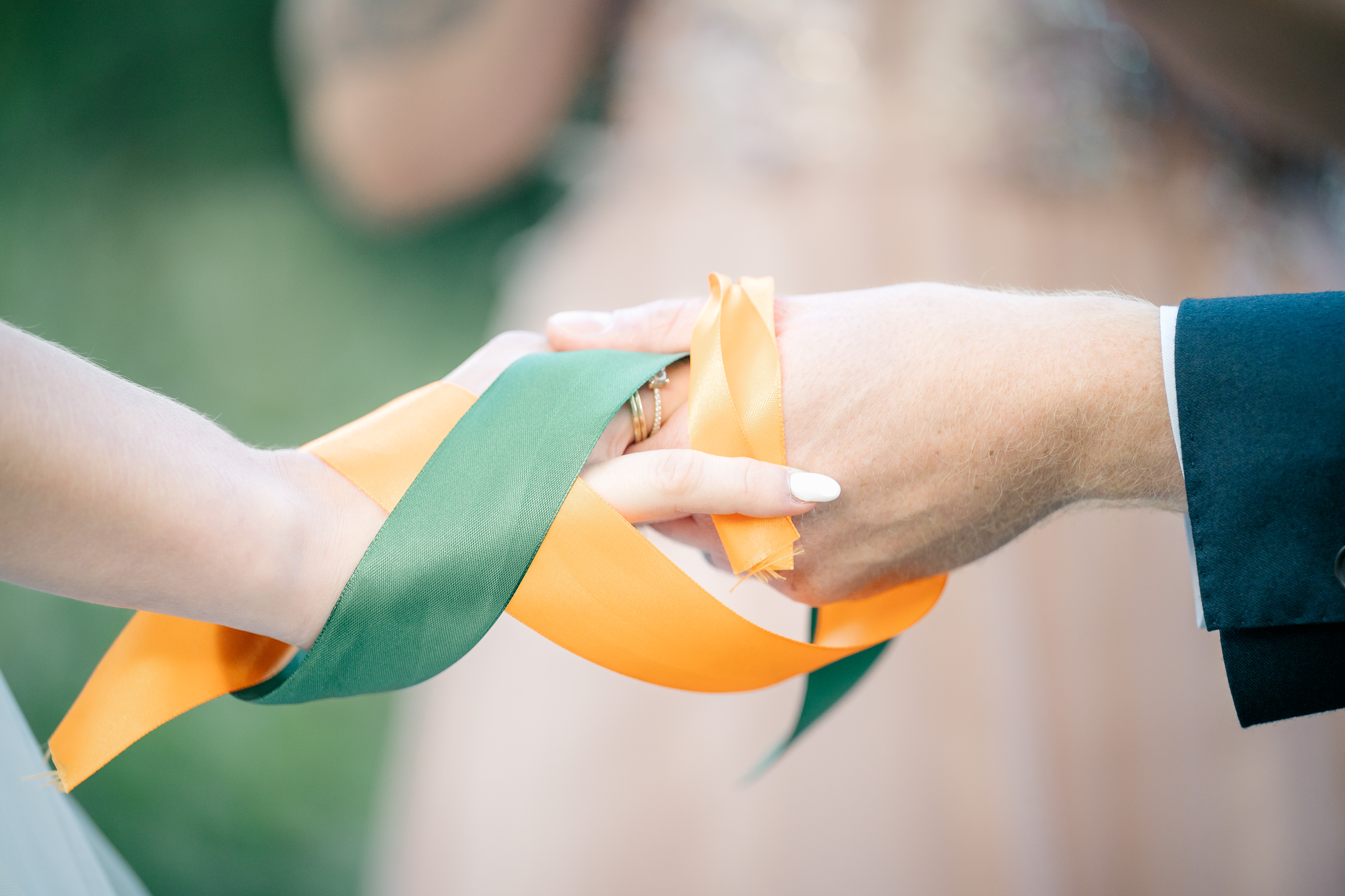close up of hand tying ceremony with orange and green ribbons wrapping the hands of the bride and groom