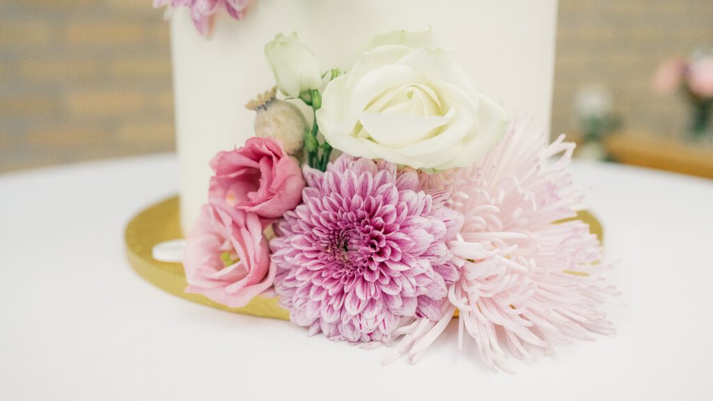 Blush and cream flowers adorn the base of a cream coloured wedding cake