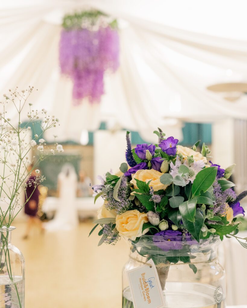 A purple and peach toned wedding reception with bouquet and a floral centrepiece of wisteria