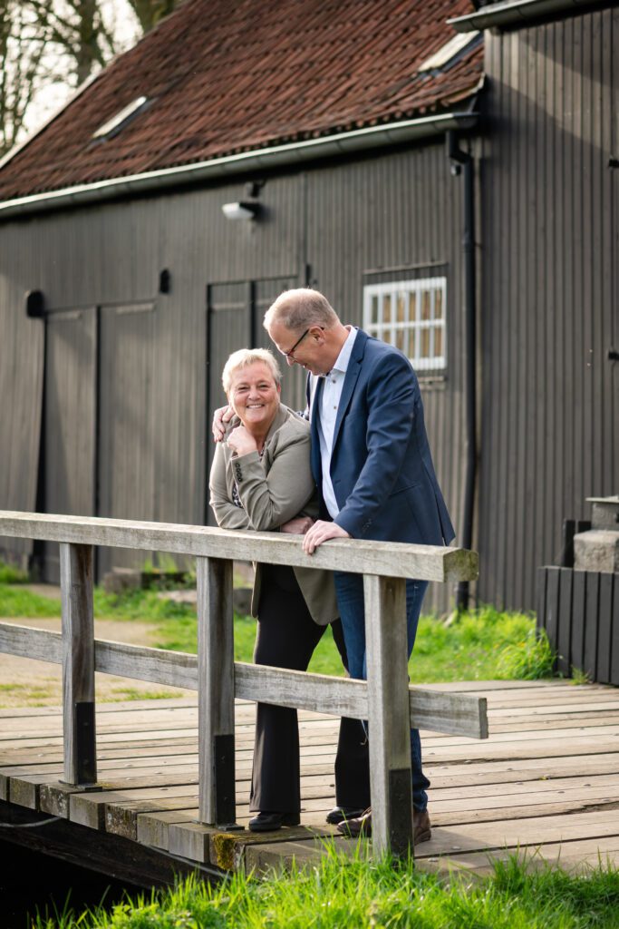 a man and a woman stand on a bridge in front of an old black watermill