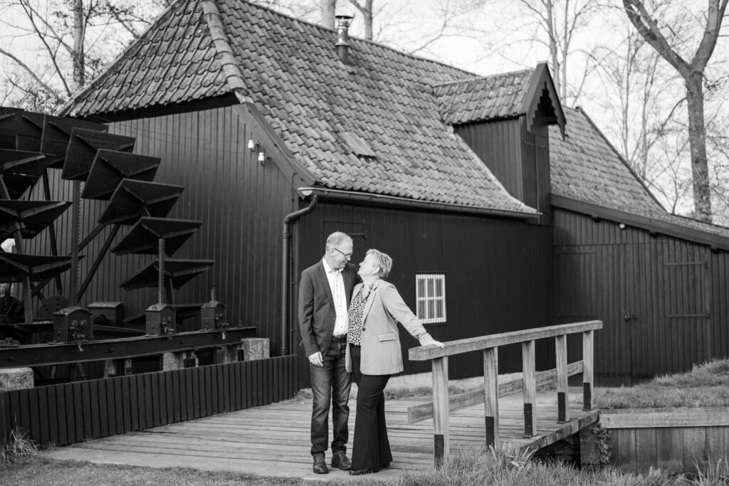 Black and white couple stands looking at each other in front of watermill