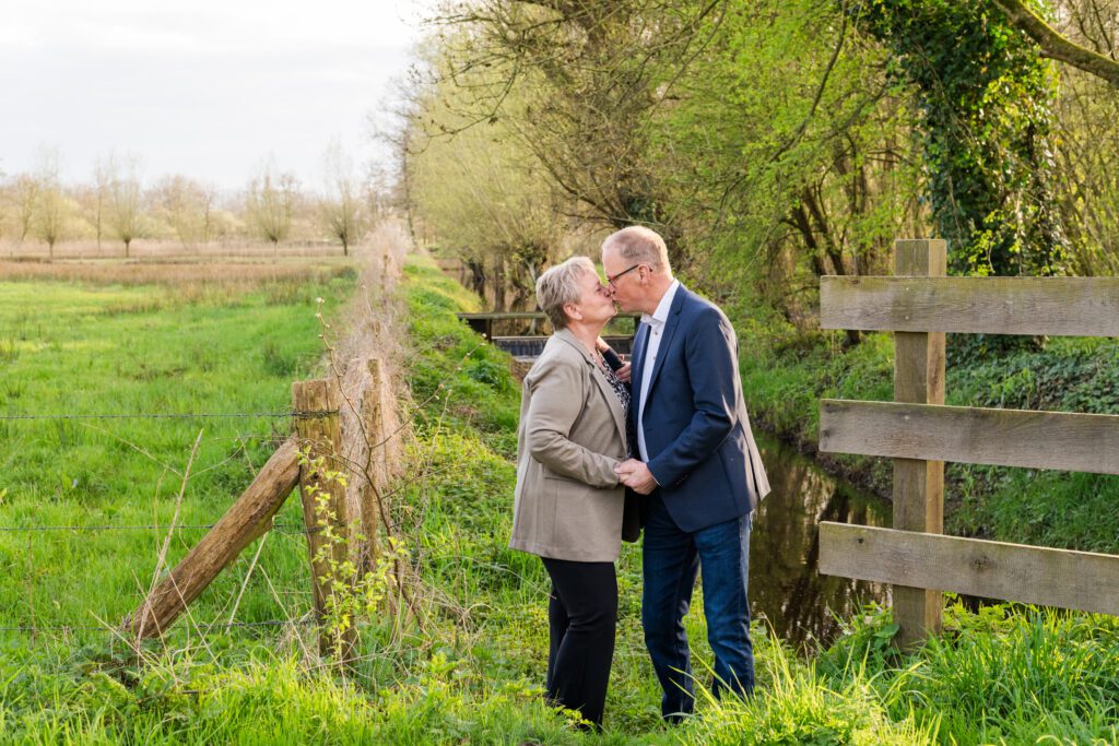 A couple stand facing each other and kissing in front of a stream and countryside by the Collse watermill